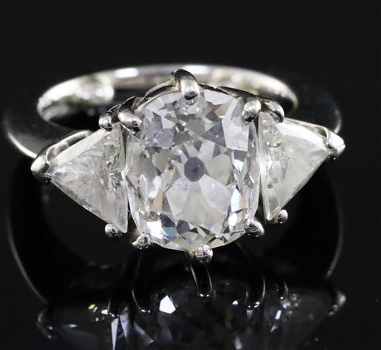 A modern platinum, oval cushion and trillion cut diamond set three stone ring, size F.